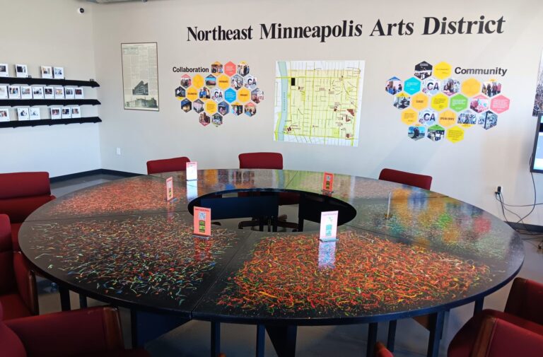 A twelve-foot circular painted table surrounded by red chairs inside the Northeast Minneapolis Arts District History Center.